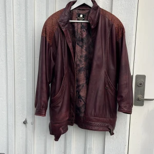 Röd skinnjacka - Snygg, vinröd skinnjacka med axelvaddar från märket Olof Nylander. Perfekt för hösten och vintern. Jackan är i strl 38 men är rätt så Oversized i modellen.
