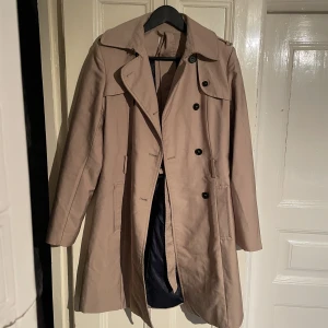 Trenchcoat med bälte  - Beige trenchcoat med bälte i midjan. I fint skick, knappt använd. Köpt i Marbella på Promod för 1500 kr ca. 
