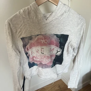 Croppad hoodie - Kort hoodie från HM. Ljusgrå/vit med motiv och text. Även text på huvan. Skicka om intresserad av fler bilder!