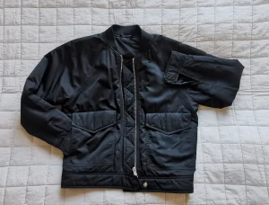 Bomberjacka Filippa K - Välanvänd, vadderad bomberjacka. Material syntet och polyester. Tvådelat blixtlås. Fickor framtill med lock och även öppen sida. Tryckknappar vid ärmslut. Ganska stor storlek, funkar även för dig som har storlek S. 