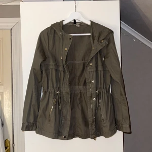 Militärgrön jacka/kappa - Kort kappliknande jacka i militärgrönt. Inga särskilda tecken på användning. Knytfunktion i midjan. Storlek 36 från H&M.