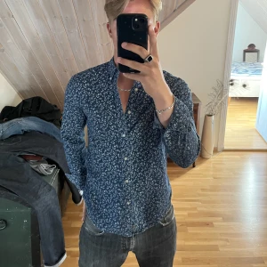 Blommig skjorta - Blå skjorta med vita blommor, säljer då den är lite liten. Storlek:M passar S Pris: 50 kr + frakt Betalning sker via Swish, skriv om ni har frågor