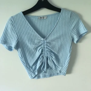 Topp/T-shirt  - En jättefin ljusblå/babyblå från NewYorker strl S passar även M. Den går att justera i mitten där fram till önskad längd. Den är använd ett fåtal gånger fläckfri och inga täcken på användning. Frakt ingår ej