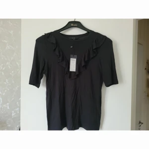 Skön bomullströja helt ny! - Svart med kort ärm och volang. Aldrig använd!