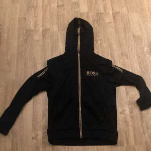 Hugo boss zip guld/svart - Tröjan är i väldigt bra skick förutom den lilla skråman den är inte använd så mycket säljer pågrund av att jag använder inte den längre priset kan ändras vid snabb affär