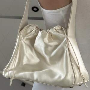 säljer denna väska i fin ljusbeige/créme silk ish material 🤍 materialet är i bra skick då jag knappast använt den :)‼️köpare står för frakten!