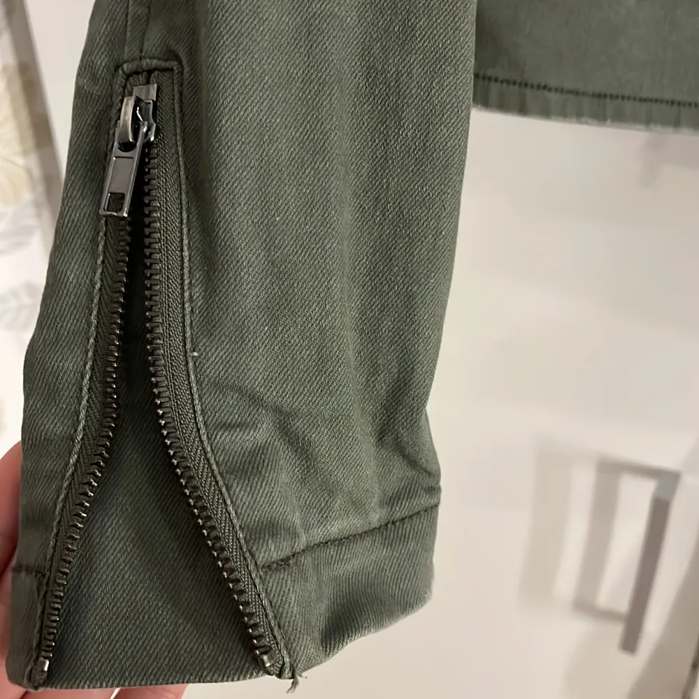 En oliv grön långärmad jeans jacka som har dragkedjor vid handleden och en sne dragkedja i mitten, sedan en normal dragkedje ficka på sidorna. Den är i bra skick och använt fåtals gånger. . Jackor.