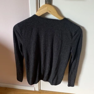 Topp med urringning på ryggen  - Mjuk och skön tröja med resår nedtill Lång modell Tyget är melerad i mörk och ljust grått  Storlek S 