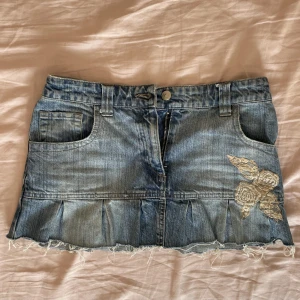 Kort jeanskjol - Minikjol i jeanstyg med en broderad blomma där fram. Den är insydd där bak, passar mig som är 165 cm och brukar ha s-m. Kan mötas upp i närheten av Mariatorget. 