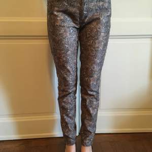 Mos Mosh Victoria Jive Pant - Metallic Choco Chip mönstrade byxor/jeans. Två framfickor, två bakfickor, dragkedja nere vid vristen, gulddetaljer. Midja är mellanväg.  Storlek: 27 Längd: 97 cm 