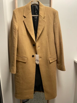Zara beige kappa - Oanvänd Zara kappa säljs pga passar inte. Ny pris 1500kr. Kappa gjord av en ullblandning. Naggad lapelkrage och långa armar. Fickor med lock på höften och en innerficka.