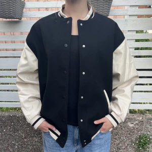College jacka oversize svart/creamvit - College jacka, oversize, svart/creamvit.  Fler bilder finns att få. Bredd armhåla till armhåla: 70cm. Längd från axel till nederkant: 68cm.  Höstjacka/vårjacka. Så gott som ny, använd fåtal gånger. Teamajacka American High School.   