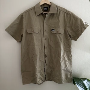 Kortärmad overshirt - Skit snygg kortärmad overshirt eller tjock skjorta. Broderad detalj på ryggen. Storleken är XL men passar mindre beroende på hur man vill ha passformen. Perfekt plagg att bara ha över en simpel t-shirt för att lyfta sin outfit