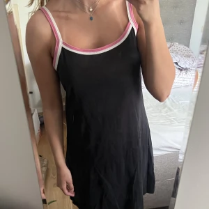 Essentials svart klänning - Svart klänning från essentials med rosa-vita band. Den har två mindre hål, men det är inget som syns när man har på sig klänningen. Storlek 42 så passar S-M💕🫶