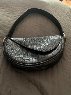 Svart handväska  - Säljer min svarta handväska i sadelmodell ifrån Nelly. Väskan stängs med en magnet knappt. Väskan är i bra skick. Säljer den för 120kr