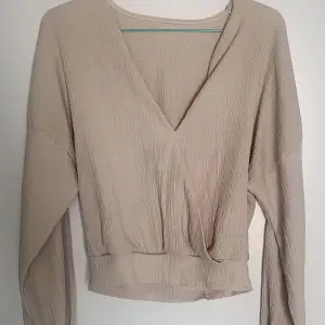 Beige blus med lång ärm, urringning och kort modell. Mycket bra skick