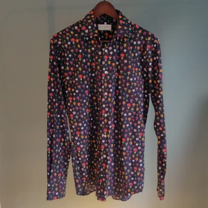 Skjorta - Mörklila, snudd på svart botten med färgglada luftballonger på gör denna skjorta stilig men lekfull. Passar i de mesta sammanhang men framförallt när man vill pigga upp tillvaron.