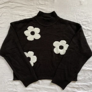 Svart stickad tröja med vita blommor - Helt ny och oanvänd med prislapp kvar. 100% akryl