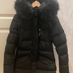 Hollies jacka, Wilma - Hollies vinterjacka, modell Wilma Long Jacket med fuskpälskrage. Både beige och svart krage medföljer.  I nyskick och endast använd ett par gånger.