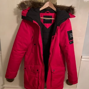 Röd PeakPerformance jacka - Röd äkta PeakPerformance parkas i bra skick, flera användbara fickor och man kan spänna huvan som man vill med bandet som man ser på bilden, pälsen går även att ta av.  Skriv om ni har frågor eller vill ha mer bilder.