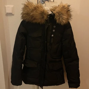 Hollies jacka - Vinter jacka dam från Hollies. Svart i stl 34. Snålt använd och i nyskick. Ej äkta päls. 