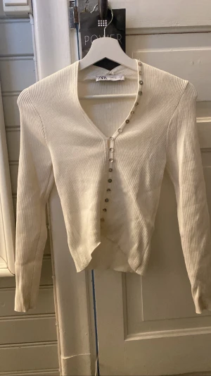 Vit ribbad långärmad med knappar - Säljer denna superfina långärmade tröjan som har knappar på magen som fortsätter upp på kragen. Aldrig använd. De står att axelbredden är 32 men tröjan är väldigt stretchig . Nypris 299kr