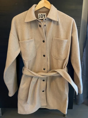 Kappa - Beige kappa från JDY. Stl.xs. Knappknäppning och skärp. Fickor i sidan. Fint skick.