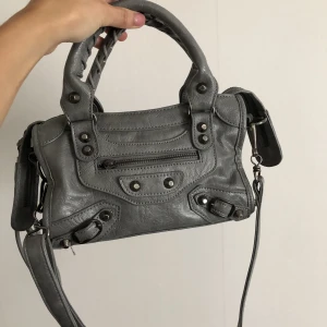 Grå handväska  - Säljer min balenciaga inspirerande väska som är i bra skick. Vet tyvärr inte märket på den. Den går både att ha crossbody och på armen. Väskan är i äkta läder. 