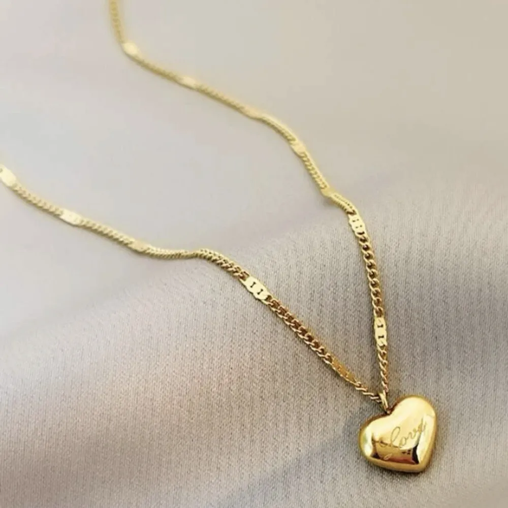 Ett guld smickrande halsband format som ett hjärta med en text lydande Love 🧡. Accessoarer.