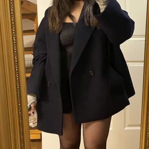 Marinblå kort kappa - Säljer min älsklingskappa från Lindex. Har använt några gånger, men fortfarande i bra skick. Kappan är i ullblandning och passar perfekt inför höst/vinter!🫶🏼Har storleken M, inte jätteoversized och jag brukar bära storlek S🫶🏼 (köptes för 1000)