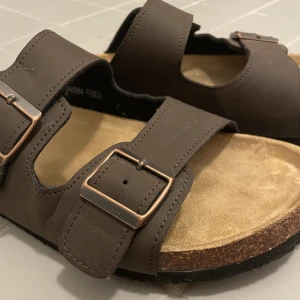 TOFFLOR - Heeejsan!☺️ Säljer ett par bekväma mörkbruna tofflor i storlek 42, pga att de var för stora. Relativt nya då de är använda ca 1 vecka.  Tofflorna har spännen med tre olika nivåer. Frakt ingår ej. 