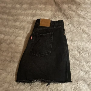 Jeanskjol - Jeanskjol i svart ”urtvättad” färg med konstgjorda slitningar från Levis. Kjolen är insydd i midjan för en perfekt fit i midjan, därav kommer den även passa en XS väldigt bra. Använd fåtal gånger, inga signifikanta defekter🤍