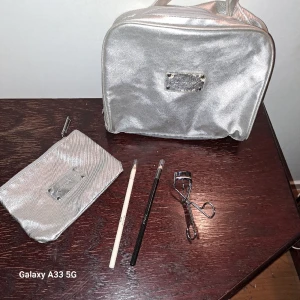 Tre kajaler två necessärer ögonfransböjare - Tre oanvända kajaler (brun som ej är med på bild, svart och vit), ögonfransböjare samt två silvriga necessärer. Dessa är I använt men gott skick, bruksslitage. Däremot finns det lite fläckar i dom efter användning.