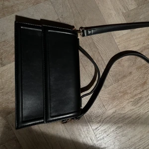 Svart handväska  - Svart handväska från Gina Tricot - använd 1 gång. Påminner om den populära modellen från Jacquemus. Det långa bandet är avtagbart