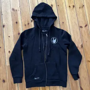 Svart munktröja eller zip upp hoddie med ett tryck av en hand som gör ett rock-tecken. Köpt på hemsidan EMP. Bra kvalitet och mjuk inuti. Det är en dammodell men passar säket alla ändå. 