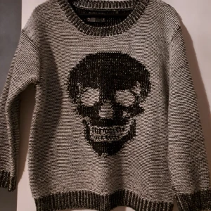 Stickad tröja med en dödskalle på - En skön tjocktröja med dödskalle mönster på.Av märket saint and mortal.Storlek M.Sparsamt använd. Inga noppor, inga skador, inga hål. Tvättad i handtvätt en gång.