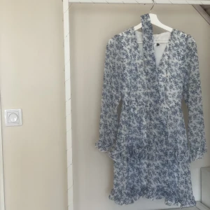 Sommar klänning  - Märke: Dennis Maglic  Storlek: S  Har drag kedja i ryggen och ett band att knyta i midjan  Använd 2 gånger  Har blåa blommor