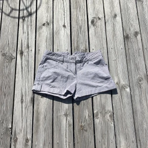 Blå randiga sommarshorts - Blå randiga lågmidjade sommarshorts med broderi POXY på framsidan och ”Remember your Roots” på baksidan. Shortsen är justerbara i midjan. Säljer då de är en aning för små för mig.