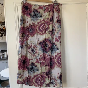 Omlottkjol - Så fin omlott kjol som knäpps med knapp och med snörning. 86 vi lång. Två lager så lite genomskinligt och sen ett heltäckande lila under. Perfekt för sommaren. I okej skick.