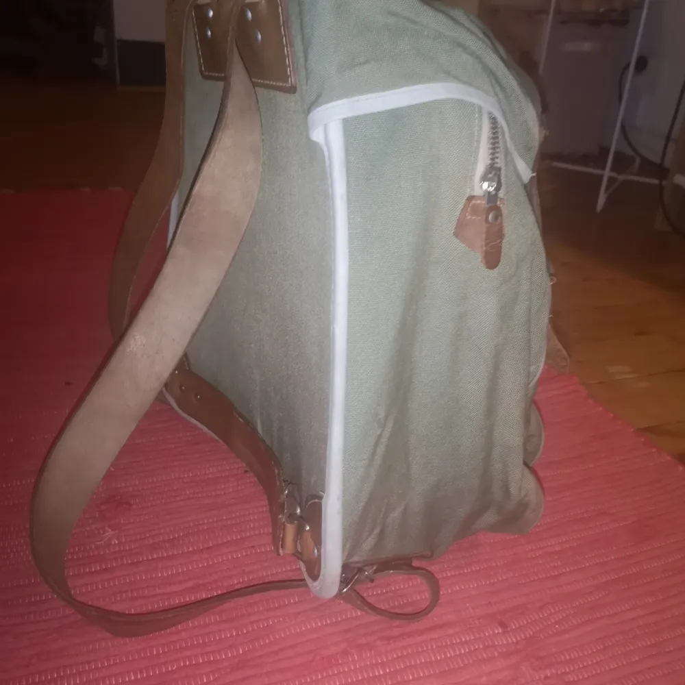 Ryggsäck med läderremmar, ryggplatta, ett litet fack och ett större. Den har några år på nacken, men den e hel och går att använda några år till. . Väskor.
