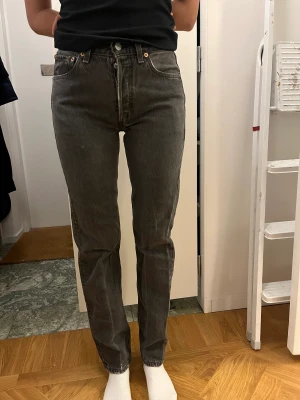 Vintage Levis 501 grå - Vintage Levis 501:or i snygg grå färg, slitningar efter användning. Storlek 29 i midjan och 34 i längd. Passar mig som annars är storlek 26 i midjan och en vanlig 36a. Hällan till knappen högst upp har gått sönder, men lagas enkelt.