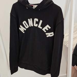 En svart moncler hoodie med vit text  Den är fake 