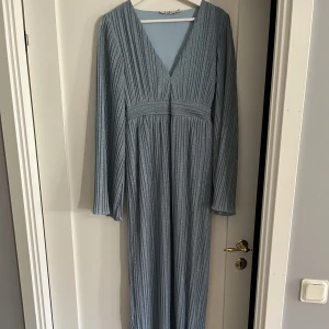 Blåglittrig långklänning   - Blåglittrig långklänning från NA-KD. Endast använd vid ett tillfälle. Urringningen är ihopsydd en liten bit men det går att sprätta upp utan problem. Originalpriset på klänningen var 799kr. Obs! Väldigt tajt i midjan (finns inga dragkedjor).