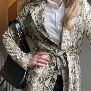 Mönstrad kappa - Tunn ormmönstrad kappa från NA-KD!🤍💛 Går att knäppa med knapparna eller knyta runt midjan med skärpet. Fickor på sidorna och slits bak. Använd en gång, mycket fint skick!