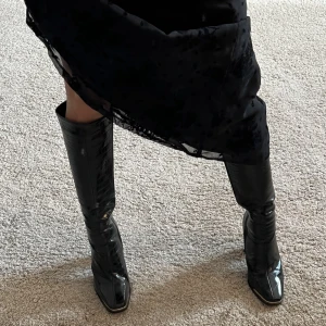 Stövlar - Svarta, knähöga boots i krokodilskinnsimitation som är använda endast en gång, därför i väldigt bra skick. Köpts från ASOS för 600kr från märket Simmi London