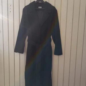 Long black Weekday coat - A light ankle length overcoat. Has three buttons and nice spacious pockets!  Size L. Length 130 cm. Shoulder width 48 cm. Underarm width 62 cm. Sleeve length (from the shoulder) 60 cm.  The shell fabric is thin, but dense and soft. Good for -3..+8°C.