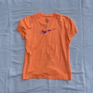 Träningströja Nike  - Orange tränings T-shirt från Nike med rosa logga! Jättesnygg och bra skick bara smått nopprig men syns knappt! Den är L i barnstorlek men funkar som en S för vuxna också. Jag har S och kan ha den utan problem.