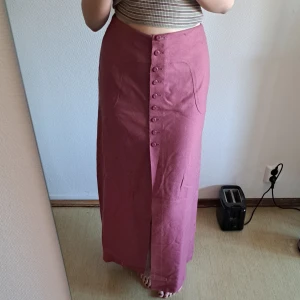 Rosa långkjol - Vintagekjol i vad som känns som en syntetblandning. Hög midja som jag vikt in på första bilden, se bild tre för hela linningen. Midjemått strax innan den höga linningen är ca 75 cm.  Färgen drar en aning åt det kallare hållet i verkligheten. 