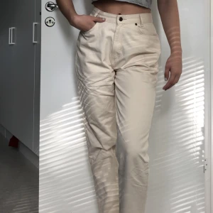 Beiga mom-chinos - Beiga avslappnade byxor i chino-likt material. Sitter åt bra i midjan men är raka och lite mer pösiga i benen, vilket gör att de liknar mom-jeans stilen.  Väldigt lätt och lent material som gör att byxorna är sköna att ha på sig. 