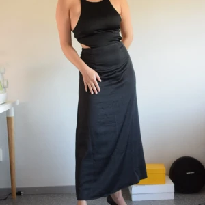 Maxi satinklänning  - Strl: M Mått: längd på kjoldelen 97cm, midja 73cm Material: 97% polyester, 3% elastan  Modell: maxiklänning, cutouts på vardera sida av midjan, snörning bak, mindre slit på baksidan  Märke: H&M Skick: fint skick, knappt använd